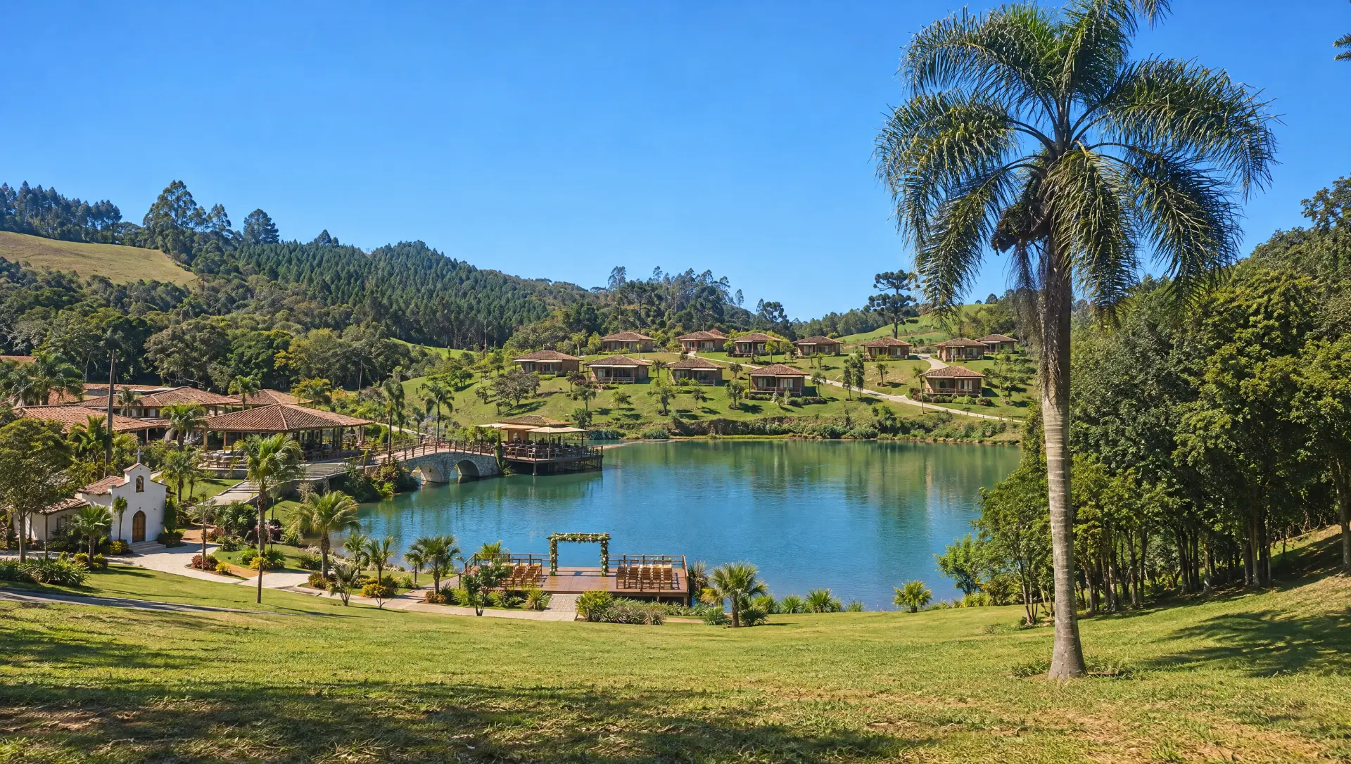 Lago em formato de gota com ponte de pedra, deck de madeira, capela e chalés ao redor