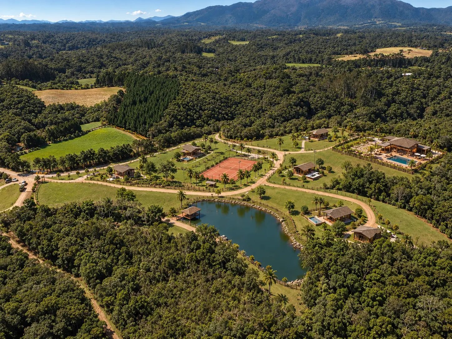 Vista aérea ampla da propriedade com o lago, as quadras, a piscina e a serra ao fundo